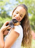 Girl in white t-shirt with black Dachshund puppy on her shoulder.