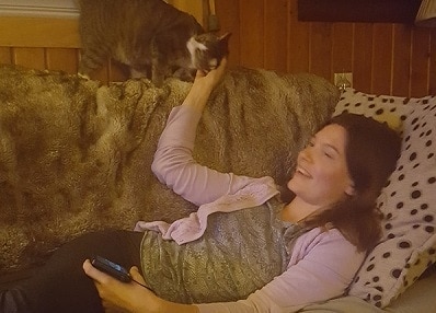 woman and cat on couch with fuzzy blanket Kvinde liggende på sofaen kæledyr kat stående over hende.