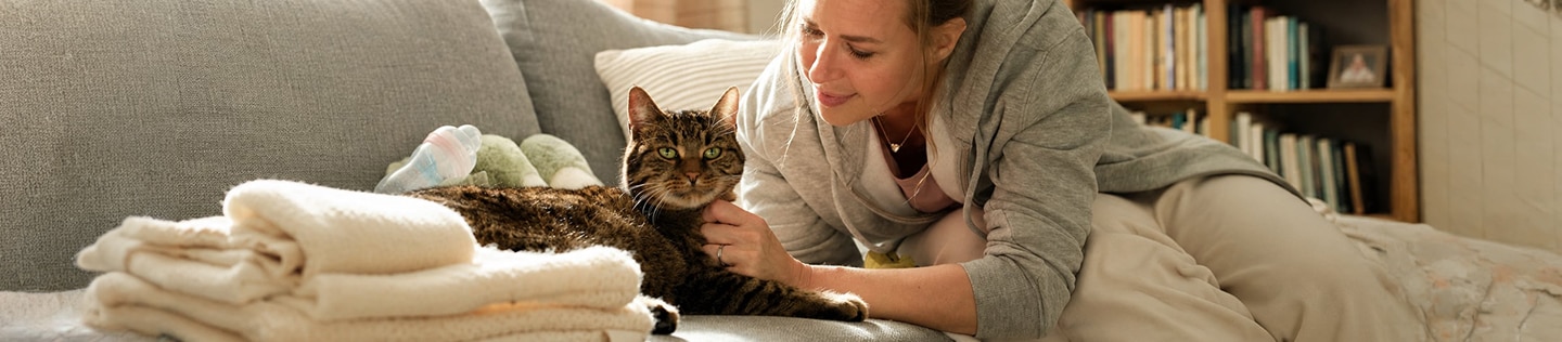 Kvinde sidder i en sofa, mens hun kæler for og taler med en tabbykat, der ligger ved siden af hende.