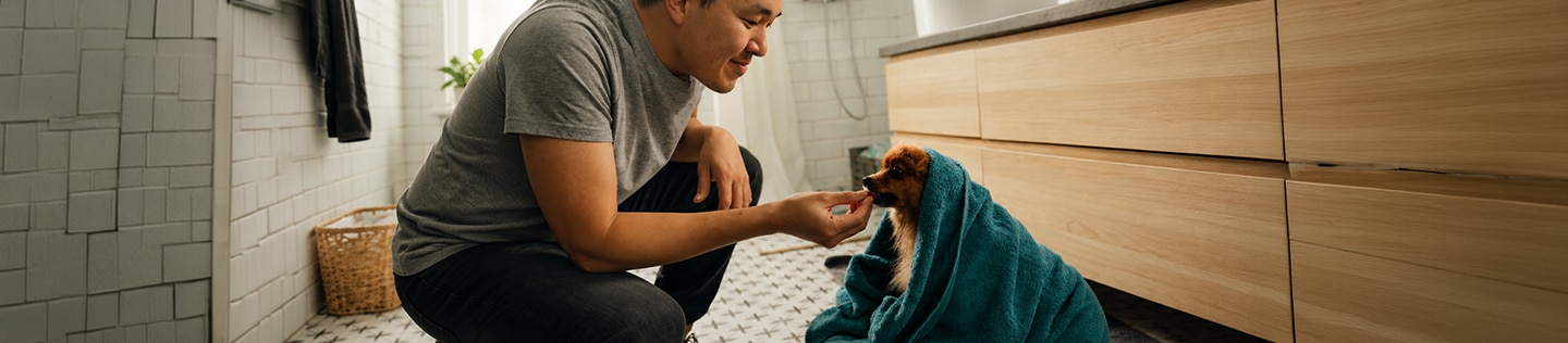 En mand, der sidder på hug og rækker hånden ud mod en racehund, der er svøbt i et blåt håndklæde